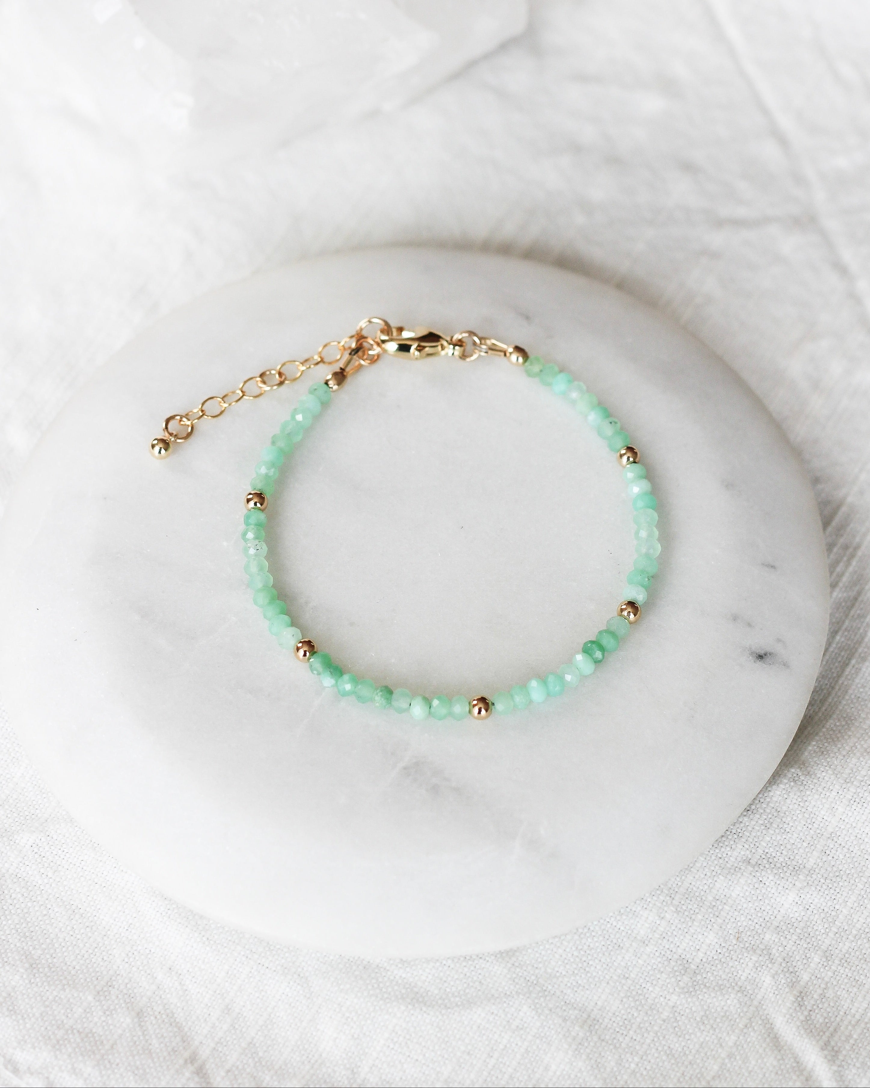 Green Chyroprase beaded gemstone bracelet with gold accents on a marble surface