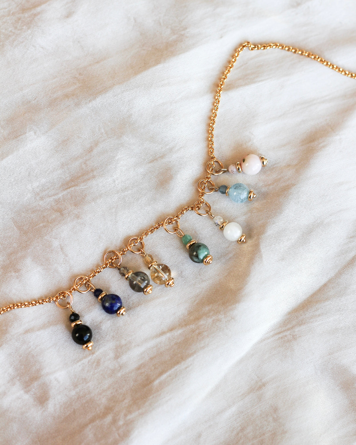 gemstone charms layered with other meaningful charms on a gold necklace.
