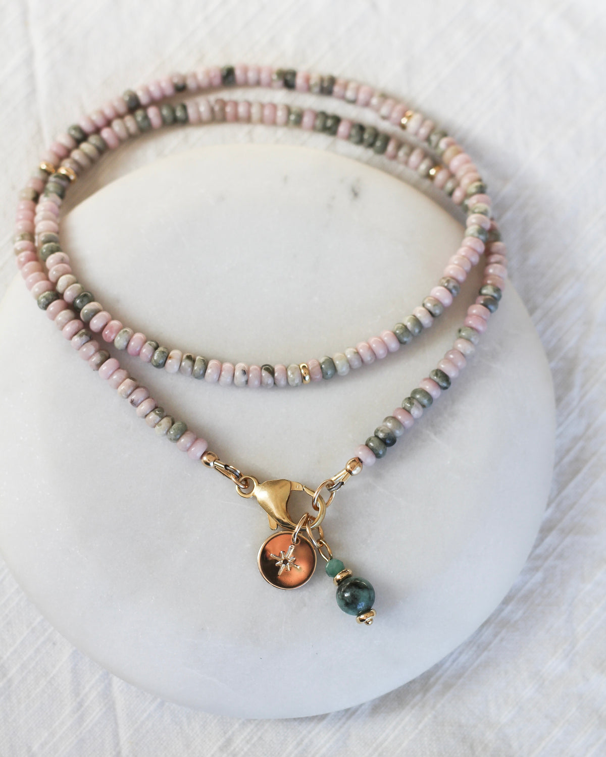Emerald gemstone charm layered with other meaningful charms on a gemstone necklace